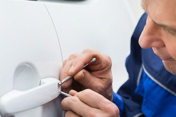 A Technician Is Opening A White Car Door With A Pair Of Picks.