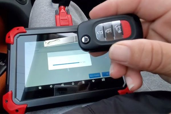 A Car Locksmith Is Holding A Car Key In Front Of A Programming Tablet.
