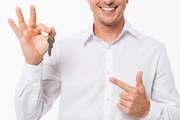 A Man In A White Shirt Is Holding A Key And Pointing At It.