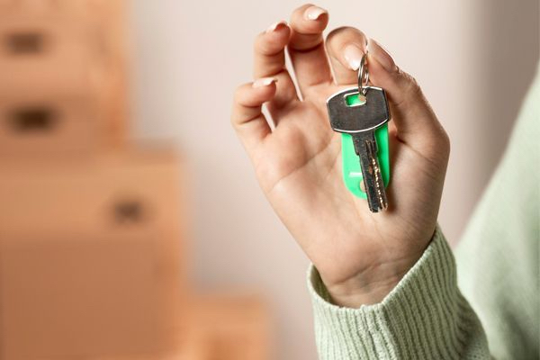 A Woman Wearing A Green Sweater Holding A Key With A Green Keychain.