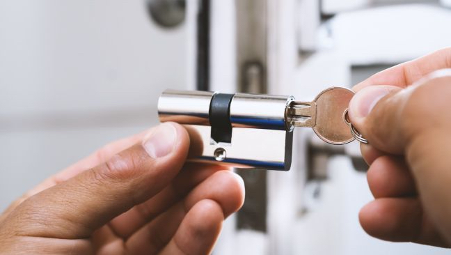 A Locksmith Is Holding A Key In A Lock Cylinder.