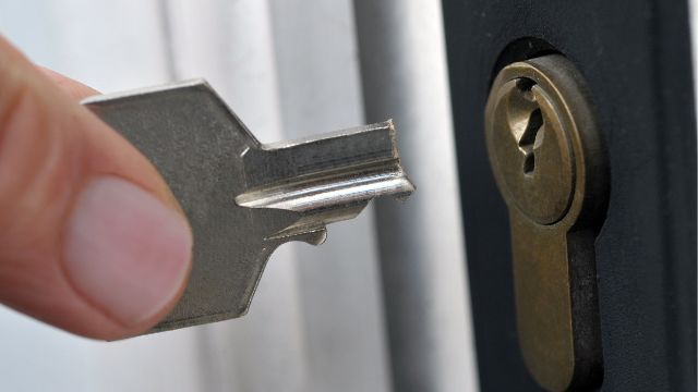 A Person Is Holding A Broken Key In Front Of A Door Lock.