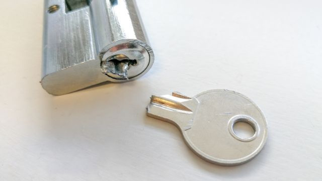 A Broken Key Is Sitting Next To A Lock Cylinder On A White Surface.