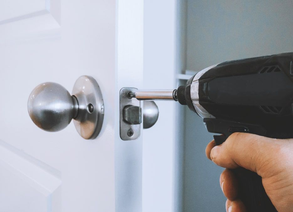 A Technician Is Installing a Doorknob Using A Black Drill.